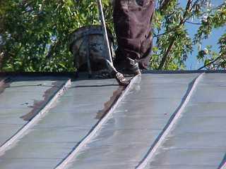 Tin roof paint is being applied by Roof Menders, Inc, starting with crimped seams